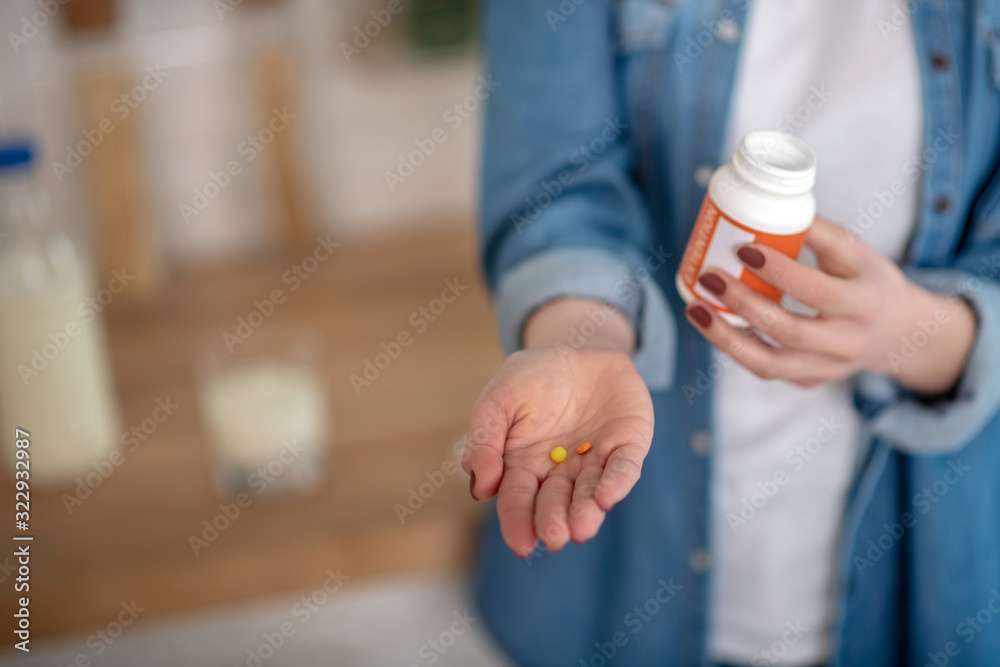 Woman holding two pills and a container in hands