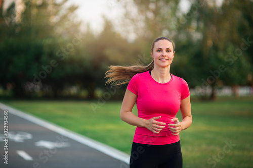 beautiful young woman runs in summer park on a treadmill