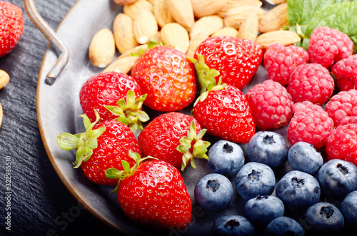 Tray with ripe organic bilberry raspberry strawberry and almonds set on slate closeup