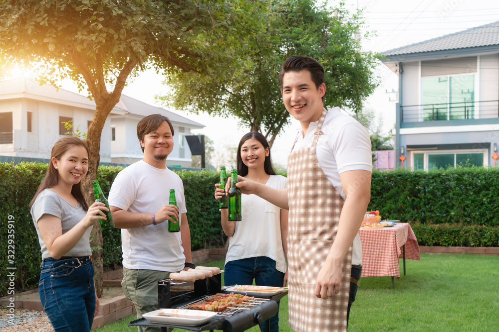 Asian man cooking barbeque grill and sausage for a group of friends to eat party in garden at home. group of friends having outdoor garden barbecue laughing with alcoholic beer drinks. Asian man cooking barbeque grill and sausage for a group of friends to eat party in garden at home. group of friends having outdoor garden barbecue laughing with alcoholic beer drinks.