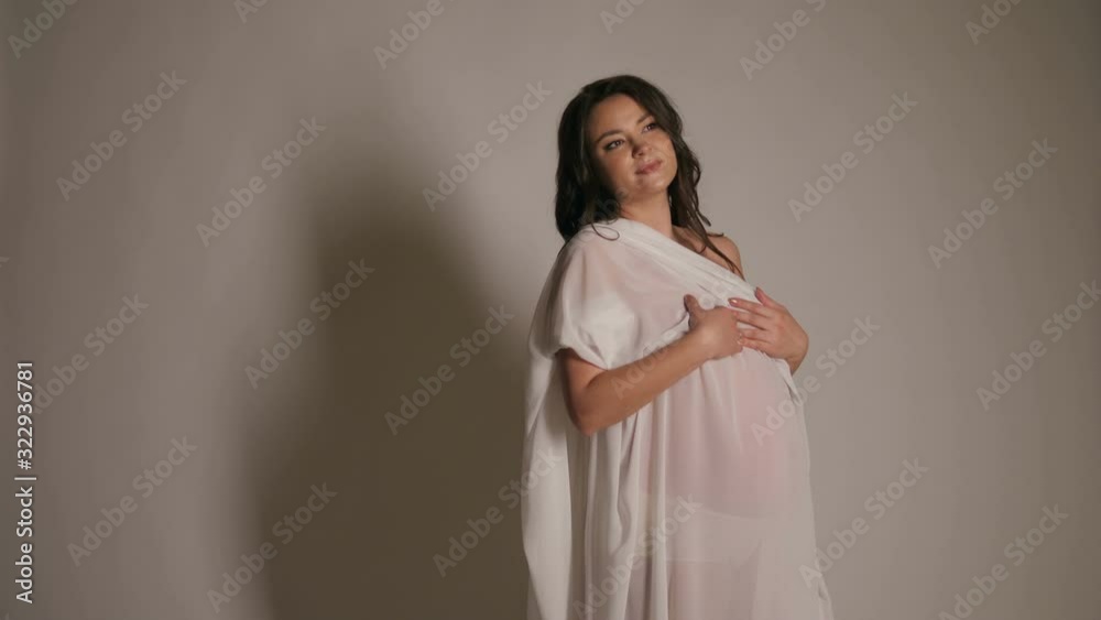 Beautiful pregnant Nude woman in white fluttering fabric on a white background. Slow motion. Portrait of a pregnant woman wrapped in a white cloth. Beautiful pregnant Nude woman in white fluttering fabric on a white background. Slow motion. Portrait of a pregnant woman wrapped in a white cloth.