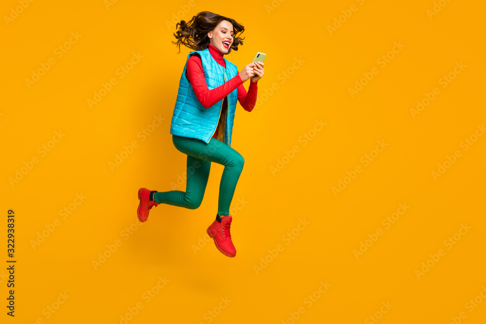 Full length profile side photo energetic crazy blogger girl jump use smartphone follow autumn season discount run wear red blue green pants trousers vest boots isolated bright color background