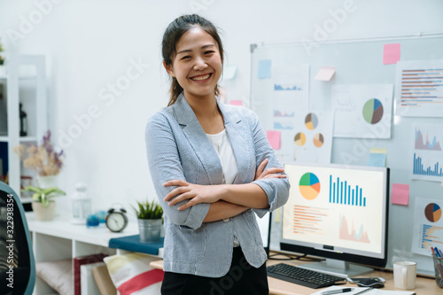 Young asian chinese woman freelancer stay indoors home office concept. confident female worker in smart casual wear with arms crossed face camera smiling with white board and documents on background.