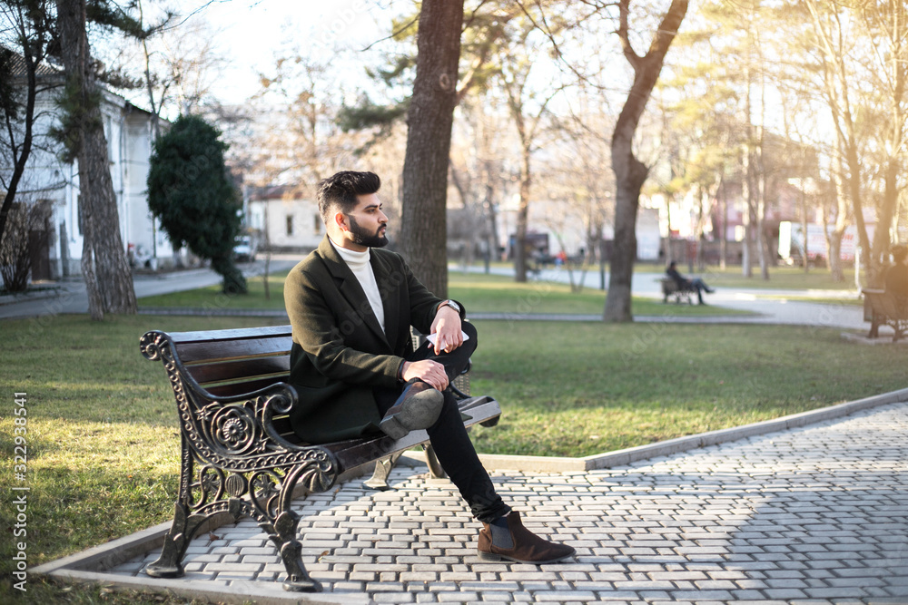 Young Indian businessman seating on the bench in park with smartphone. Young Indian businessman seating on the bench in park with smartphone.