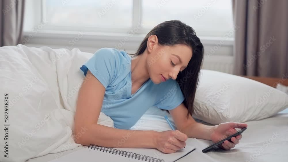 beautiful girl writes in exercise book lying on the bed beautiful girl writes in exercise book lying on the bed