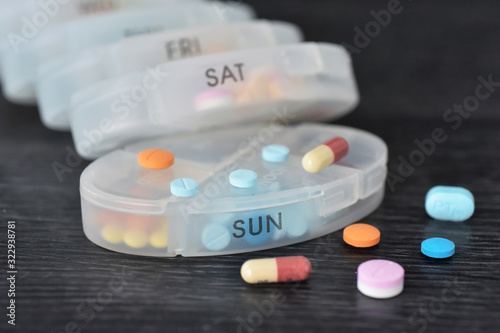 Stacking daily pill box with colorful pills inside and outside on black background