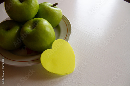 On the white table is a plate with green apples, next to a yellow sticker for the inscription