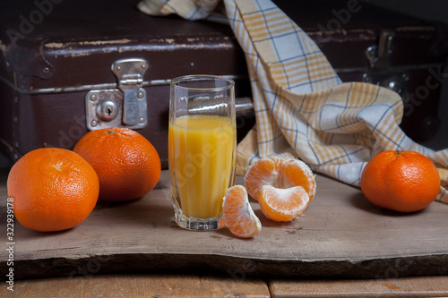 Unpeeled round ripe orange mandarins or tangerines, slices of peeled mandarin and glass of fresh juice on wooden board.
