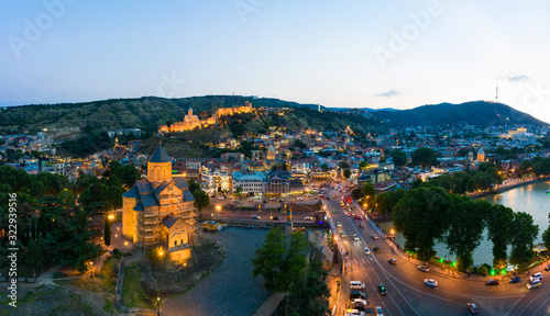 The evening panorama of the old town in the old district of Avlabari, Holy Trinity Cathedral and Rike Park, the Kura river reflects the evening city lights in Tbilisi, Georgia.