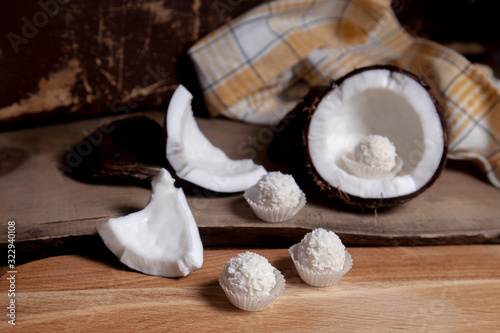 Coconut with white pulp and white candies on wooden background..