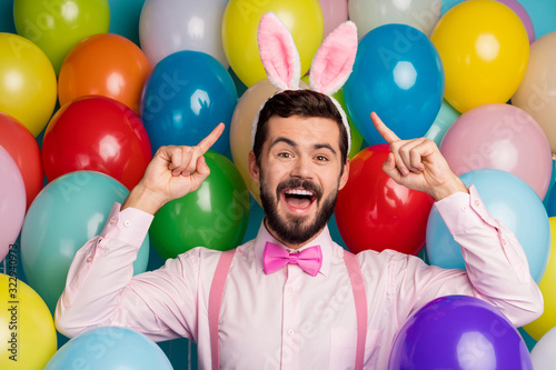 Photo of funny cool guy colorful decor easter festive party mood direct fingers head wear pink shirt bow tie suspenders fluffy bunny ears on balloons creative design background