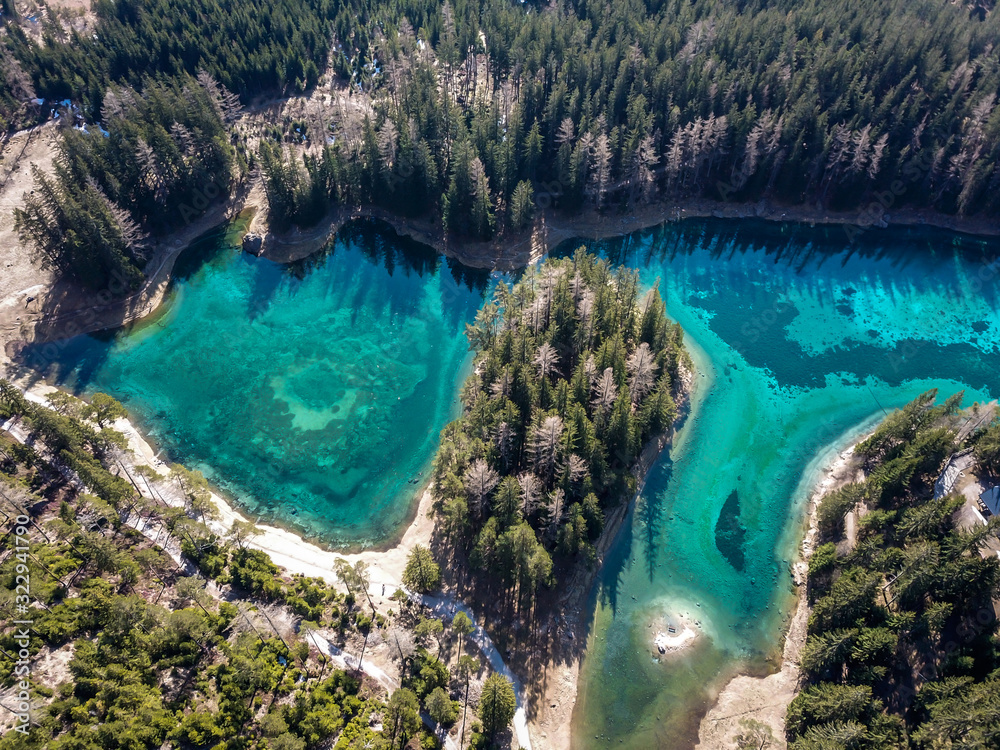 Obraz premium A drone shot of anAlpine valley in Austria. The valley has a Green Lake in the middle. A headland in the middle of the lake. The algae give the lake distinctive color. Early spring in the mountains