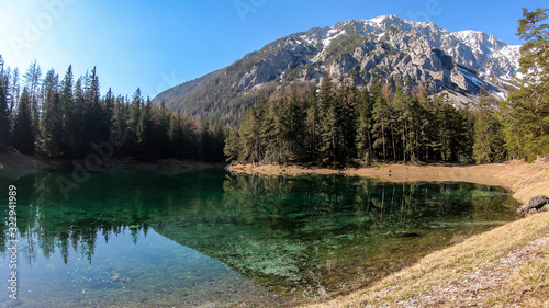 Fototapeta Naklejka Na Ścianę i Meble -  A peaceful view on an Alpine valley in Austria. The valley has a Green Lake in the middle. Early spring in the mountains. There is a high mountain range in the back. Freshness. Few ducks on the lake.