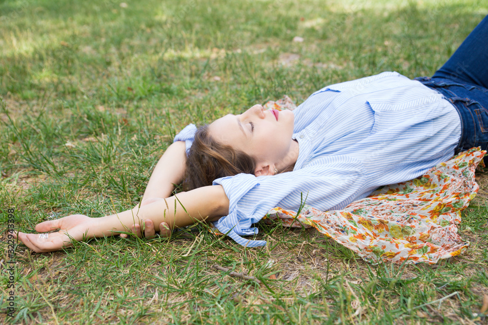 Relaxed young woman lying on headkerchief on ground in park. Beautiful lady relaxing outdoors. Leisure, relaxation concept Relaxed young woman lying on headkerchief on ground in park. Beautiful lady relaxing outdoors. Leisure, relaxation concept