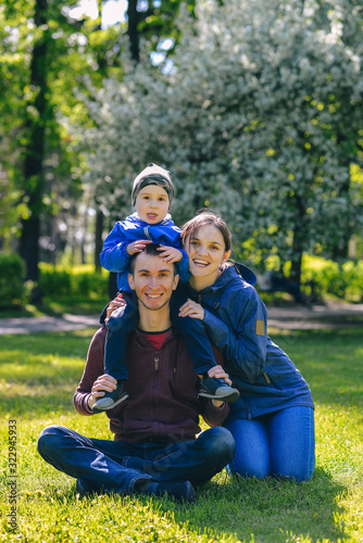 Happy family together in outdoor park at spring sunny day. Mom, dad and son in the garden. Group of people on green grass