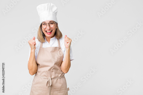 Fotografia middle age baker woman feeling shocked, excited and happy, laughing and celebrat