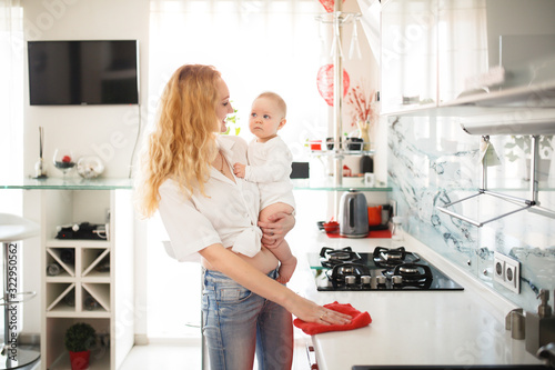 Photos Mom with baby in her arms in sling cleans kitchen