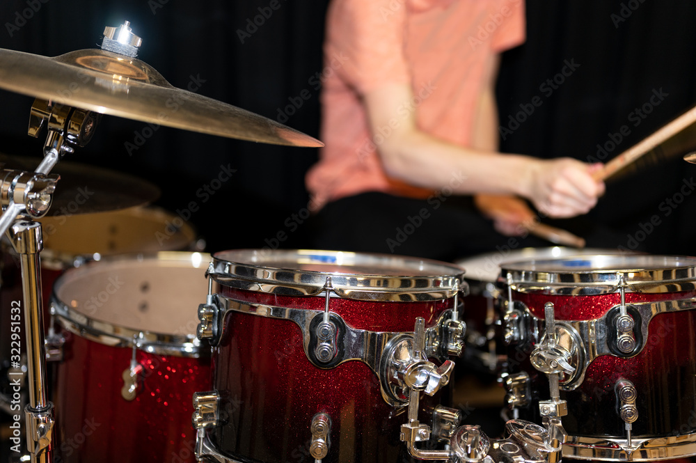Red glittering drum set with golden cymbals with a man in orange t-shirt playing drums behind it. Red glittering drum set with golden cymbals with a man in orange t-shirt playing drums behind it.