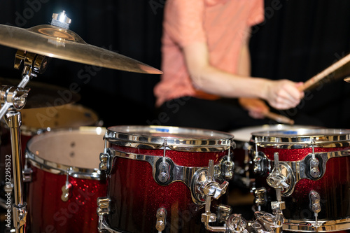 Red glittering drum set with golden cymbals with a man in orange t-shirt playing drums behind it.