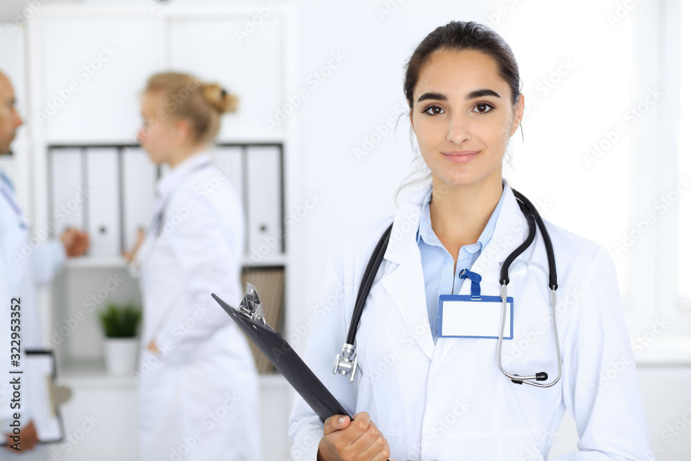 Doctor woman in clinic with colleagues at the background. Hispanic or latin american staff in medicine Doctor woman in clinic with colleagues at the background. Hispanic or latin american staff in medicine