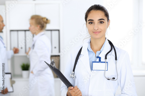 Doctor woman in clinic with colleagues at the background. Hispanic or latin american staff in medicine