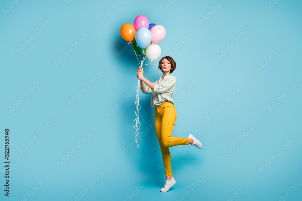 Full size profile photo of funny lady surprise birthday party hold many air balloons playful weekend mood wear casual green shirt yellow pants footwear isolated blue color background Full size profile photo of funny lady surprise birthday party hold many air balloons playful weekend mood wear casual green shirt yellow pants footwear isolated blue color background