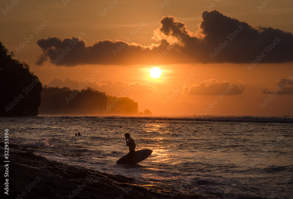 Surfer walking out of the water in Bali, Indonesia during the sunset