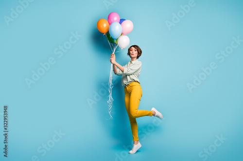 Full size profile photo of funny lady surprise birthday party hold many air balloons playful weekend mood wear casual green shirt yellow pants footwear isolated blue color background