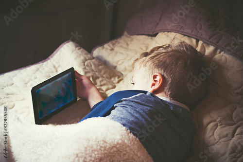 Small kid using digital tablet while relaxing in the bedroom.