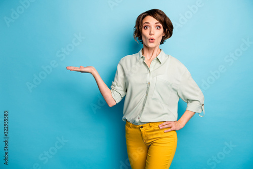 Photo of pretty funny lady hold open arm empty space novelty sale product unbelievable low price wear casual green shirt yellow trousers isolated blue color background