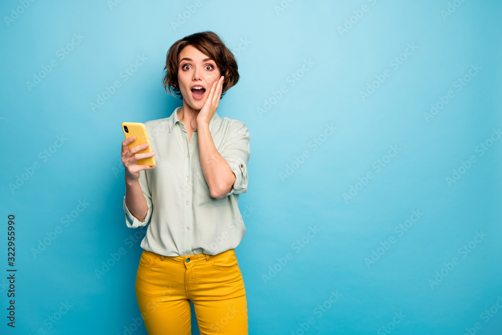 Photo of pretty lady hold telephone open mouth read positive comments followers reaction arm on cheekbone wear casual green shirt yellow trousers isolated blue color background Photo of pretty lady hold telephone open mouth read positive comments followers reaction arm on cheekbone wear casual green shirt yellow trousers isolated blue color background