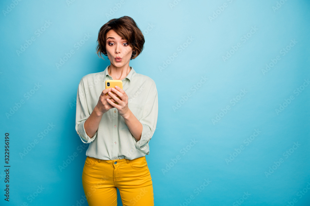 Photo of attractive lady hold telephone hands read new blog post comments not believe eyes speechless wear casual green shirt yellow trousers isolated blue color background - obrazy, fototapety, plakaty 