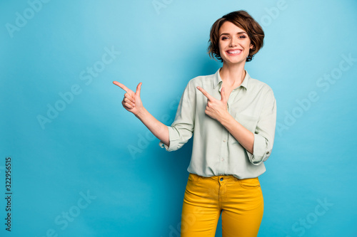 Photo of funny beautiful lady short hairdo indicating fingers empty space advising cool low prices shopping wear casual green shirt yellow trousers isolated blue color background photo