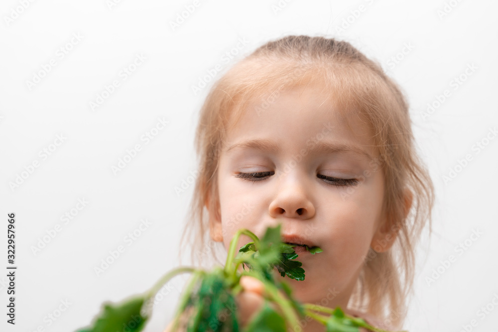 little girl in a light T-shirt holds a bunch of parsley in one hand and bites off, the girl in blur little girl in a light T-shirt holds a bunch of parsley in one hand and bites off, the girl in blur