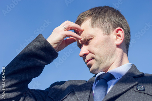 portrait of a man in a coat with a thoughtful look against the blue sky, holding his head with one hand (portrait of the Creator) photo