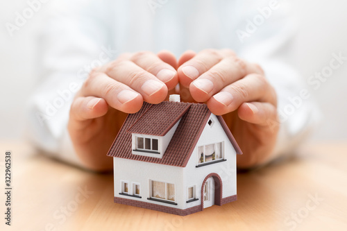 Property insurance. House miniature covered by hands