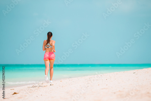 Fit young woman doing exercises on tropical white beach in her sportswear