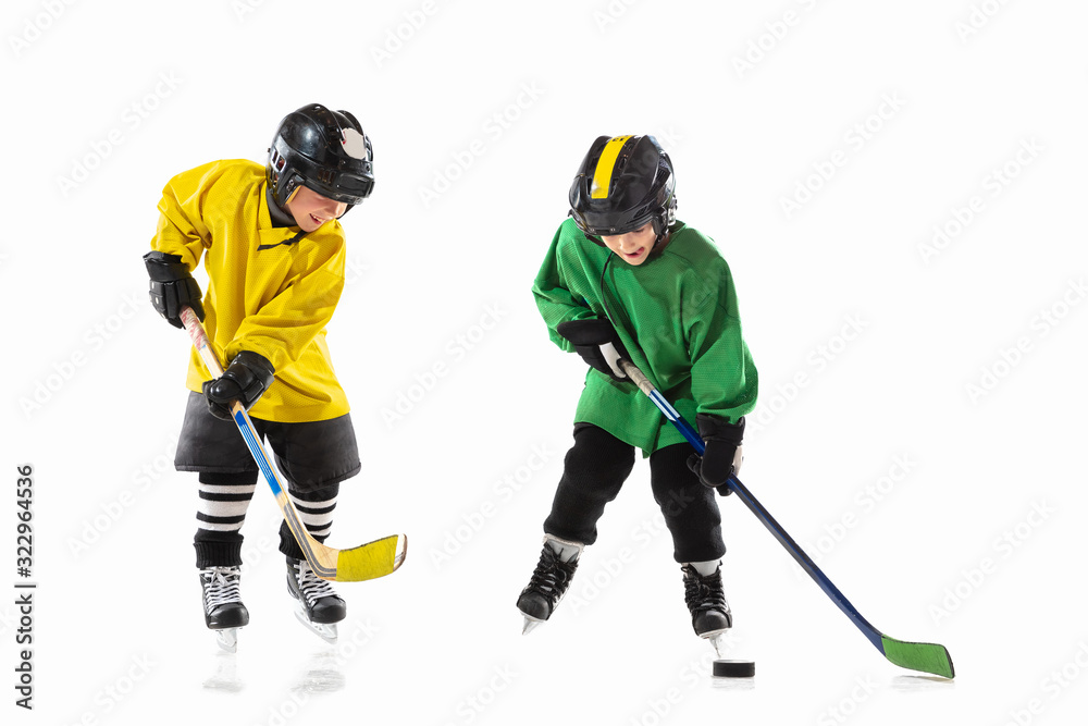 Fototapeta premium Little hockey players with the sticks on ice court and white studio background. Sportsboys wearing equipment and helmet practicing. Concept of sport, healthy lifestyle, motion, movement, action.