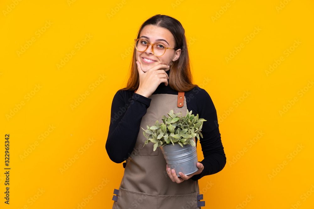 Young gardener girl holding a plant over isolated yellow background thinking an idea Young gardener girl holding a plant over isolated yellow background thinking an idea