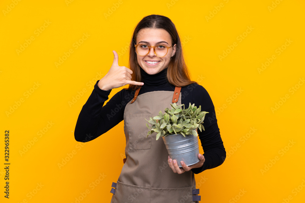 Young gardener girl holding a plant over isolated yellow background making phone gesture Young gardener girl holding a plant over isolated yellow background making phone gesture