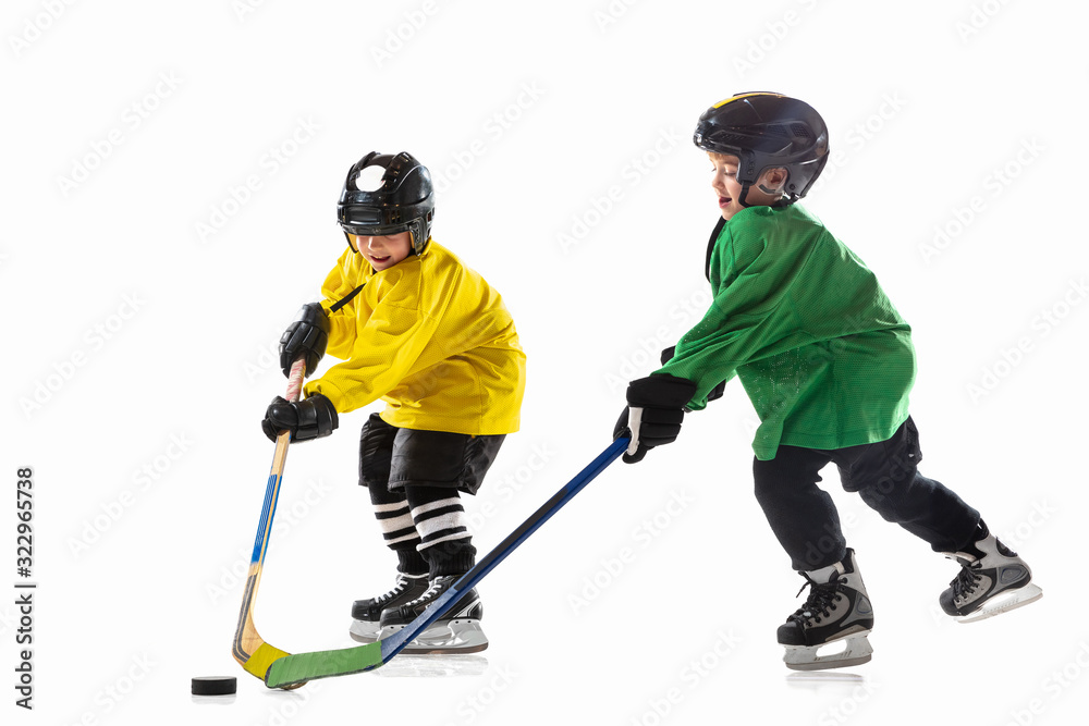 Fototapeta premium Little hockey players with the sticks on ice court and white studio background. Sportsboys wearing equipment and helmet practicing. Concept of sport, healthy lifestyle, motion, movement, action.