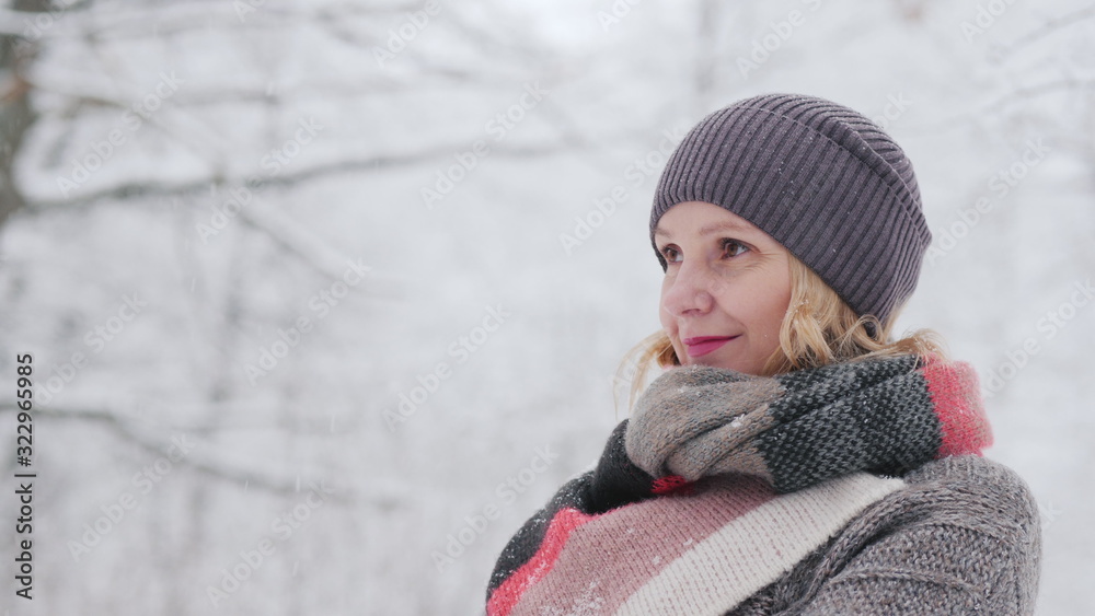 Side view of A woman in a warm sweater and a bright scarf stands in a snow park Side view of A woman in a warm sweater and a bright scarf stands in a snow park