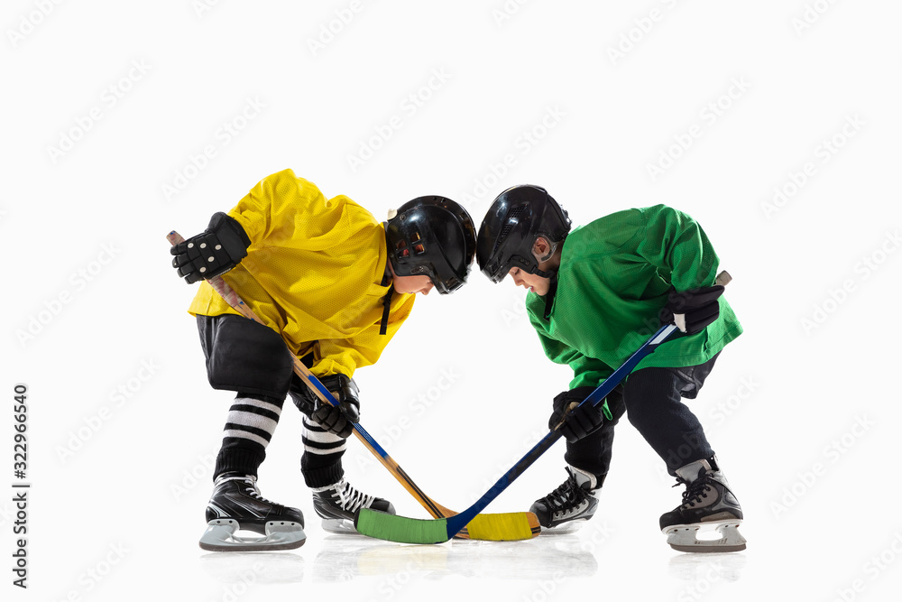 Obraz premium Little hockey players with the sticks on ice court and white studio background. Sportsboys wearing equipment and helmet practicing. Concept of sport, healthy lifestyle, motion, movement, action.