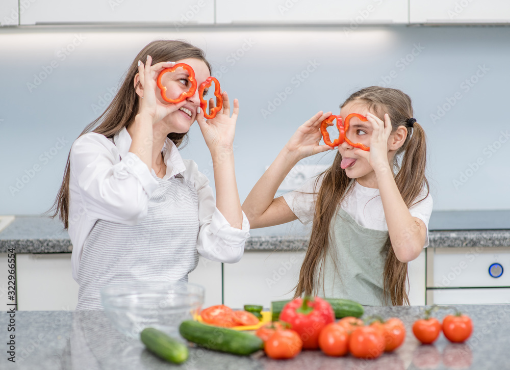 Mother and child preparing healthy food and having fun, holds a pepper in front of their eyes like a glasses Mother and child preparing healthy food and having fun, holds a pepper in front of their eyes like a glasses
