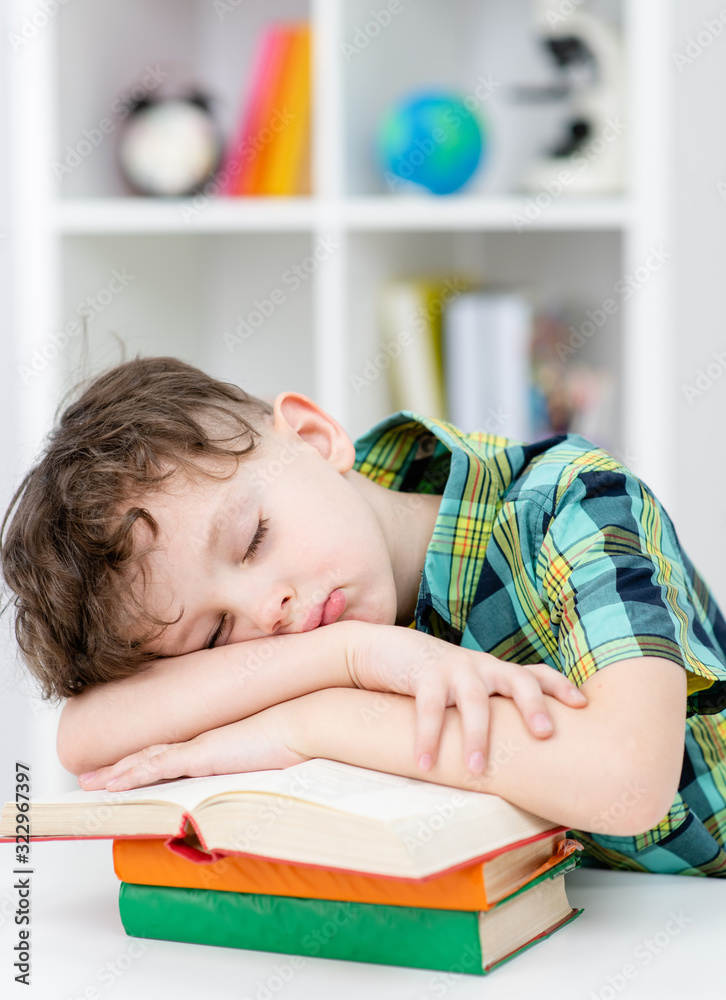 Tired young boy sleeps on a books at classroom in a school Tired young boy sleeps on a books at classroom in a school