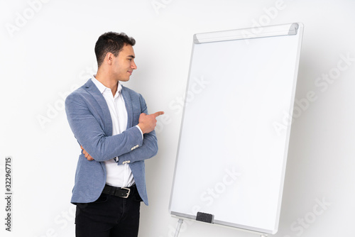 Young caucasian handsome man isolated on purple background giving a presentation on white board and pointing it