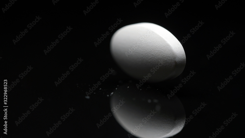 white tablet with a reflection on a black background. The concept of medication.