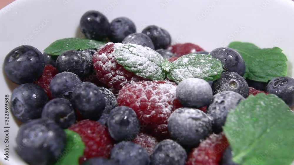 Blueberries in powdered sugar with mint leaves. Bio fruits, healthy eating, vegan food, diet. Fresh berries in a white bowl sprinkled with powdered sugar close-up. Blueberries in powdered sugar with mint leaves. Bio fruits, healthy eating, vegan food, diet. Fresh berries in a white bowl sprinkled with powdered sugar close-up.