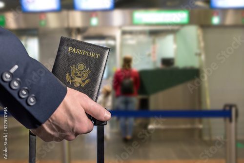 Man (businessman) in a blue suit with suitcase holding american passport in the airport opposite Immigration and passport control. concept. America. USA