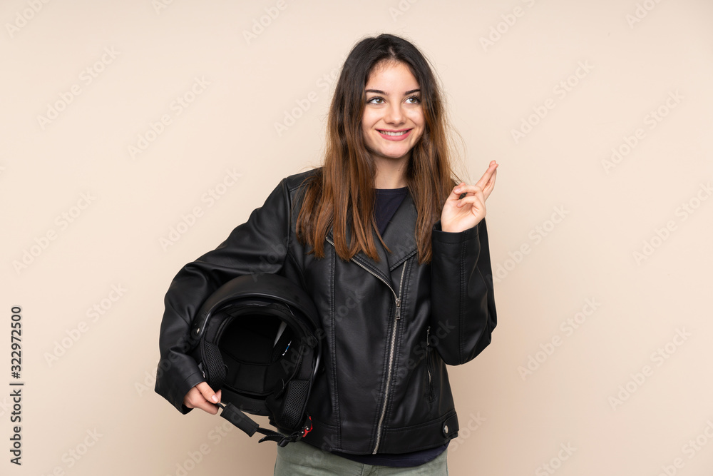 Woman with a motorcycle helmet isolated on beige background with fingers crossing